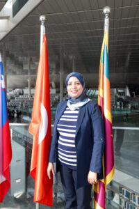 A picture of a woman in a headscarf standing with flags in the background