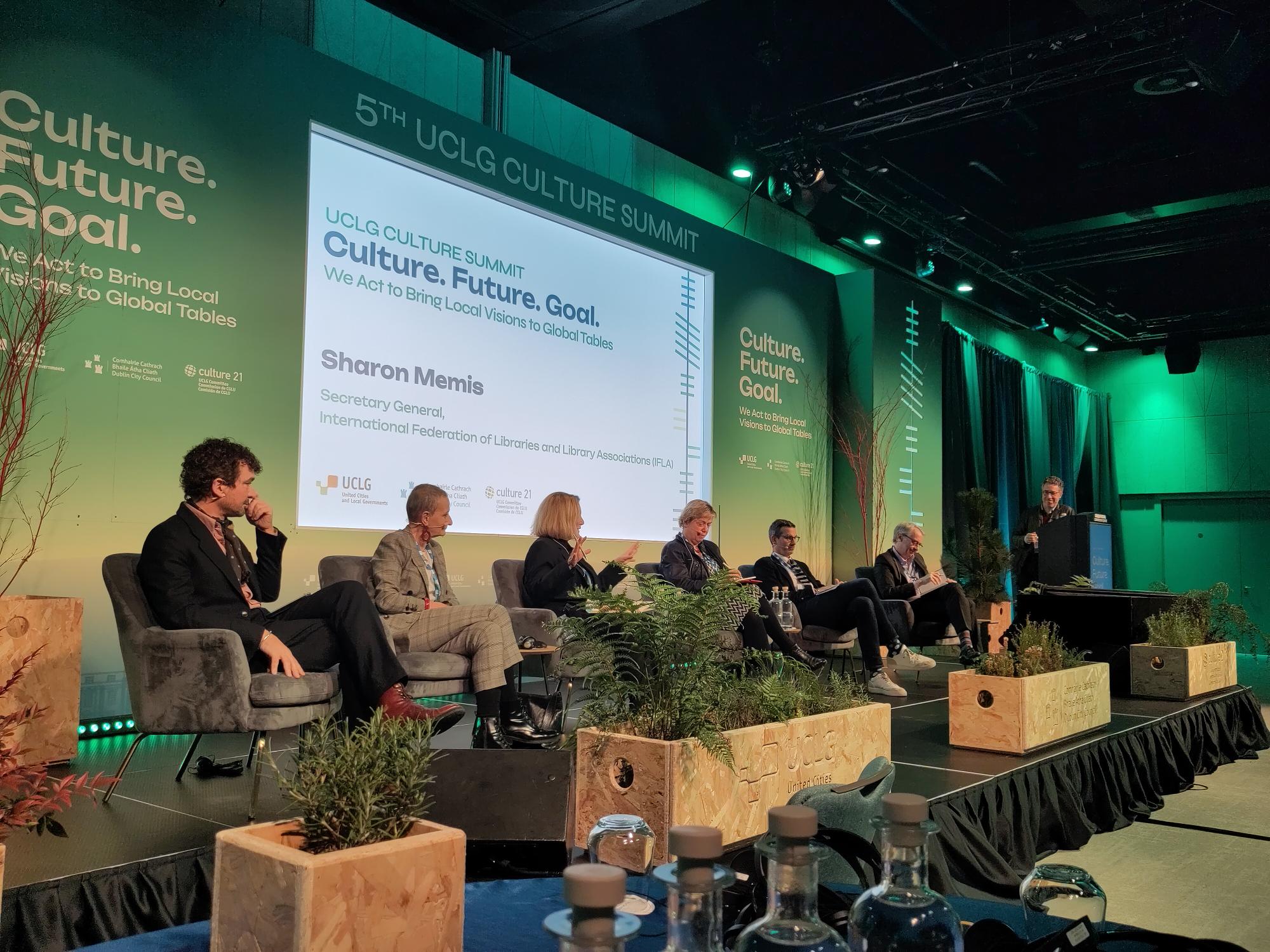Picture of a panel at the UCLG Culture Summit - six people on a podium with a powerpoint behind and plants in front