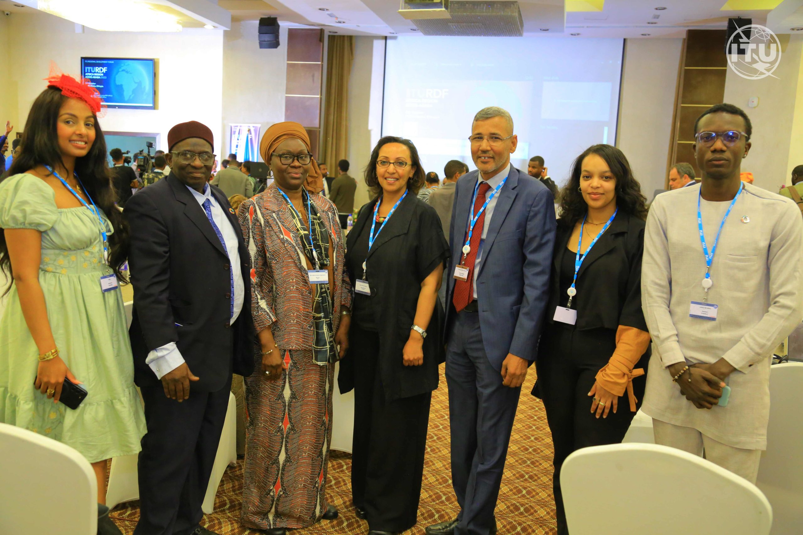 Damilare Oyedele with other participants scaled Group of delegates at the International Telecommunications Union Regional Development Forum, Africa. Left to right, a woman in a green dress with a red flower in her hair. A man with a red hat. a woman in a patterned shirt and top, a woman in black, a man in a blue suit with a red tie, a woman in black, and a man in a beige top and trousers.