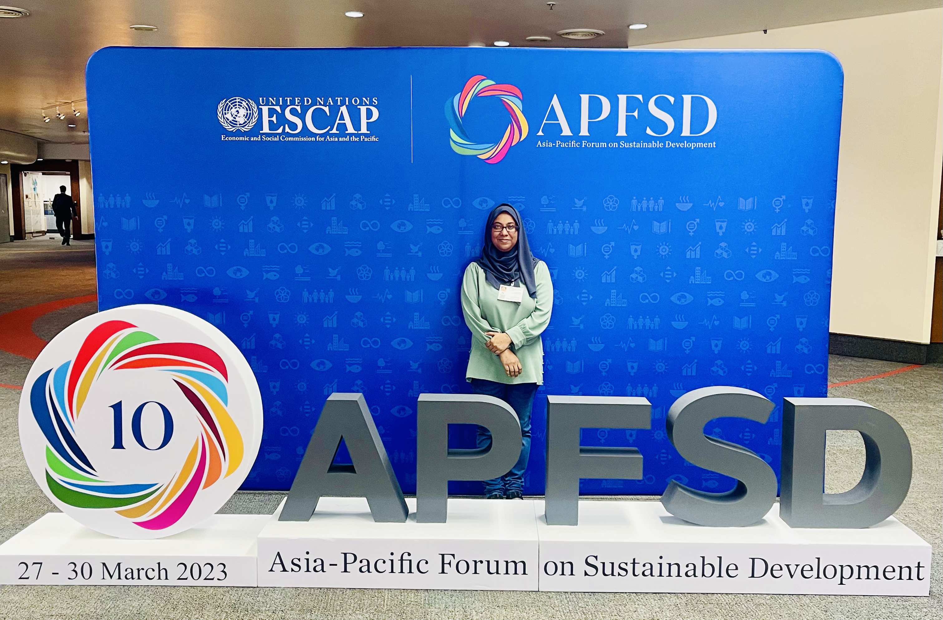 IMG 5536 IFLA representative Fathimath Nashfa standing behind a 10th Asia-Pacific Forum on Sustainable Development logo, with a blue background