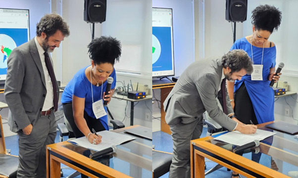Picture of a man in a grey suit and a woman in a blue dress signing an agreement