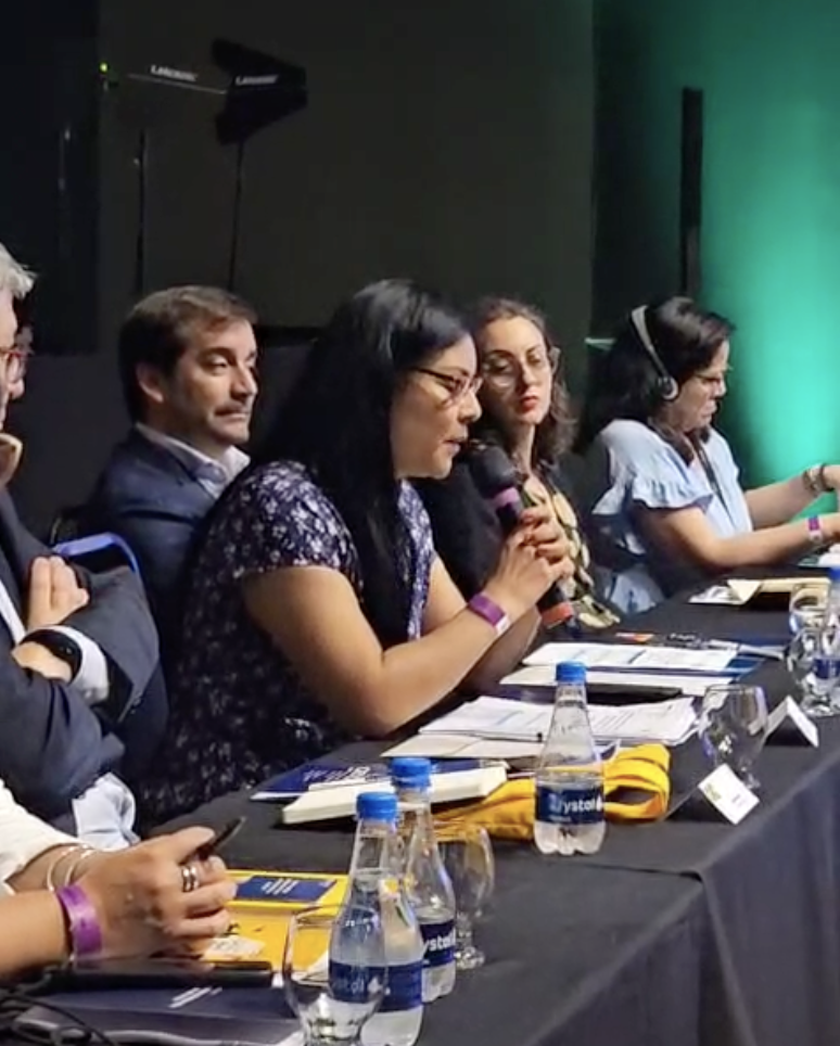 Roxana Huaman Huriarte speaks into a microphone at the CERLALC Ministerial meeting, with others sitting left and right of her