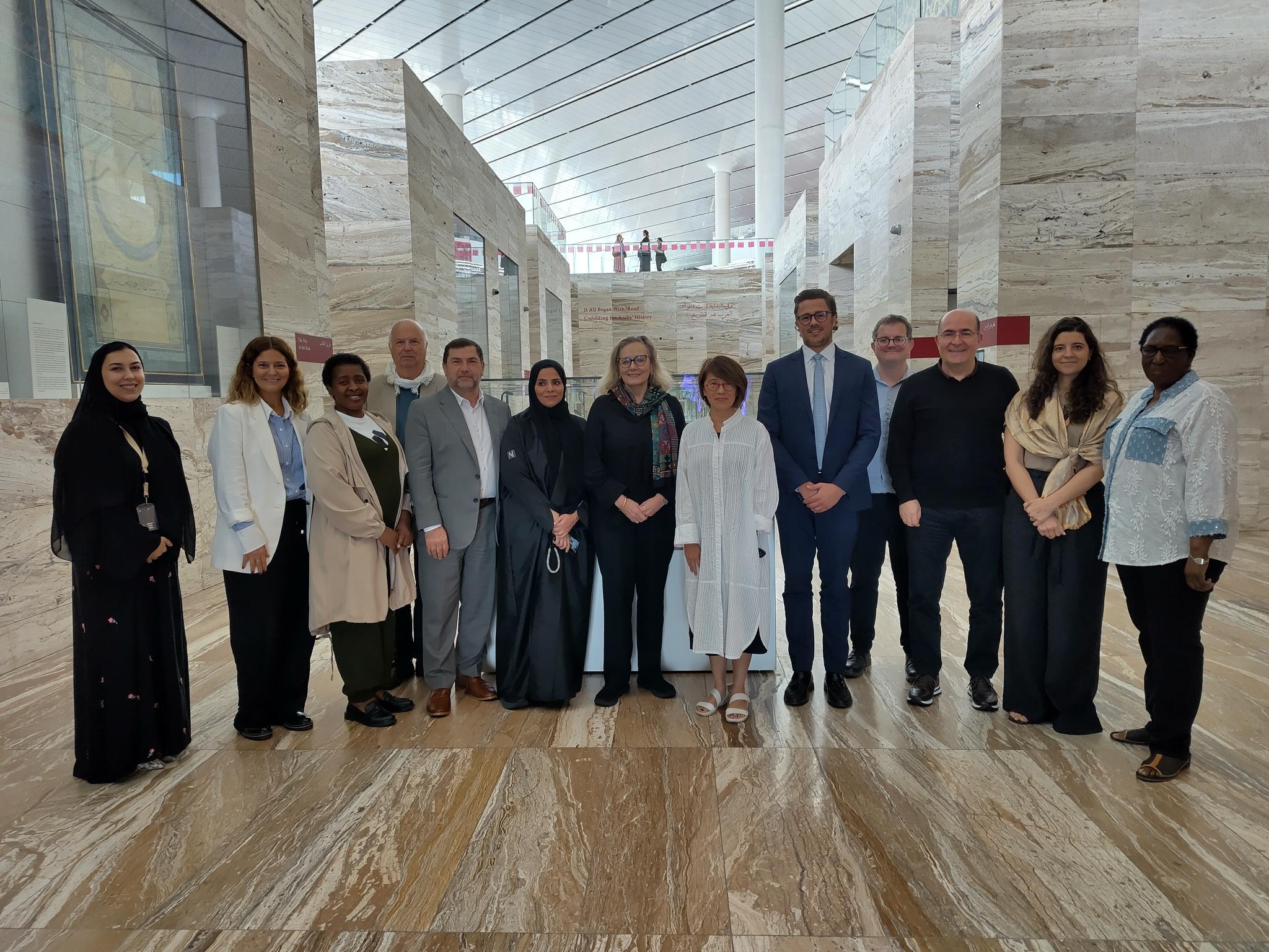Group of people standing in a marble space with exhibits behind them, and a roof open to a wider building