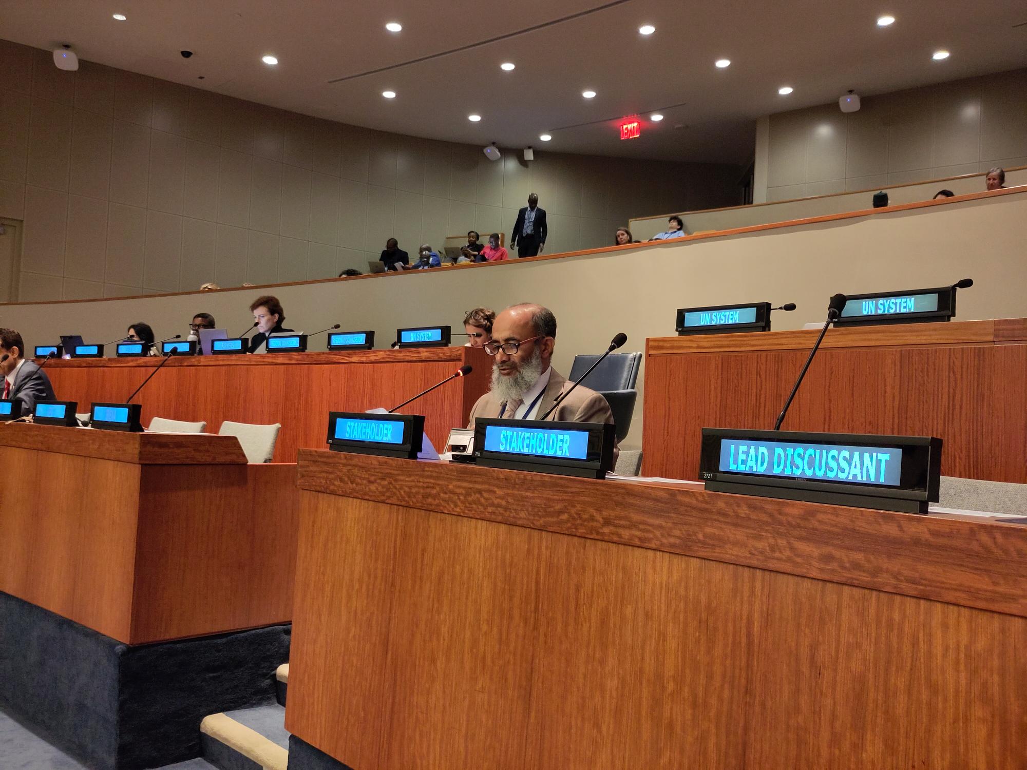 A man with a beard speaking into a microphone behind a table