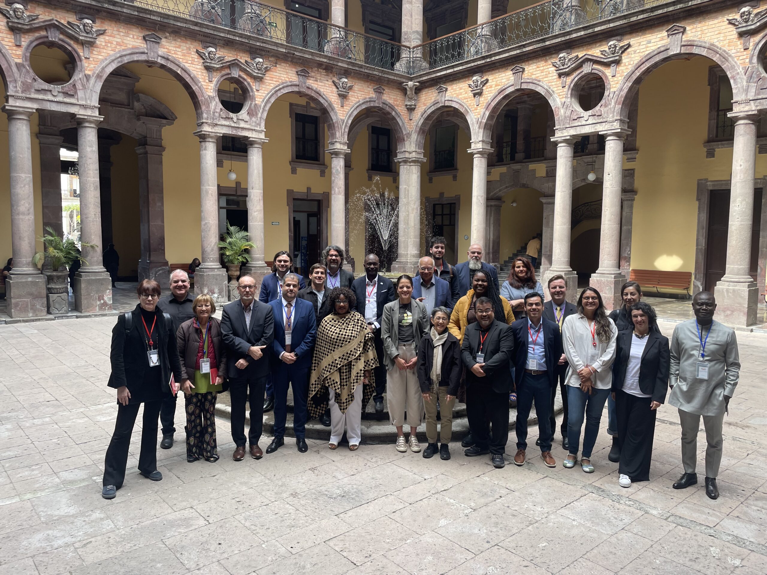 Group of around 20 people of different backgrounds, standing in the courtyard of a building with classical architecture with Mexican touches