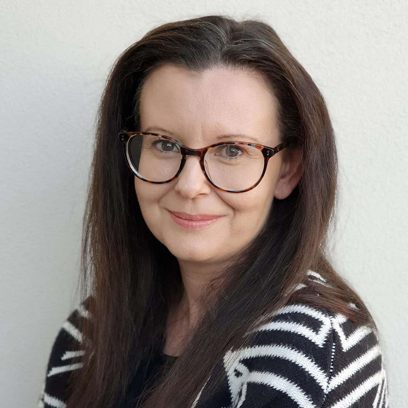 Photo of a woman with dark brown long hair and glasses, and a striped black and white top